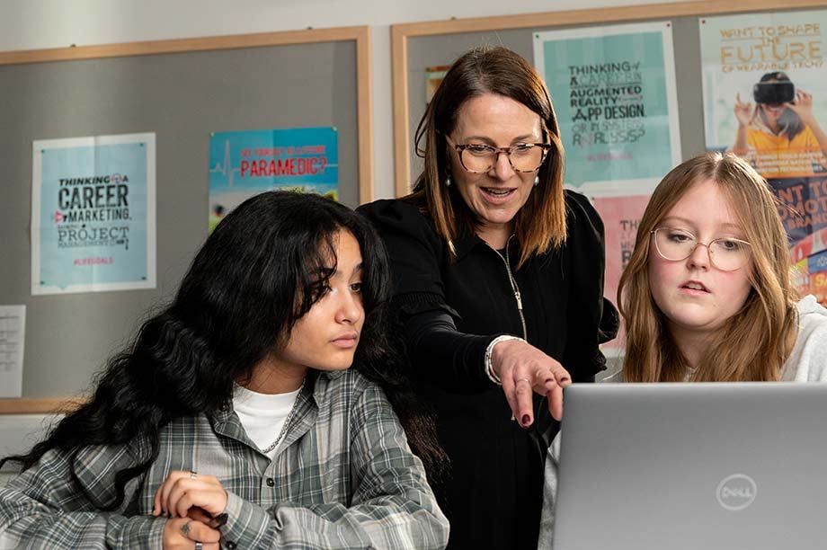 Teacher pointing to laptop with students onlooking