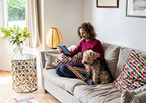 Wellbeing - Lady and her dog relaxing on the sofa reading tablet