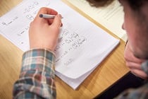 A Level Maths student working on paper using formula